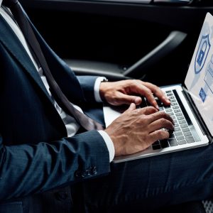 partial view of african american businessman using laptop with internet security illustration in car